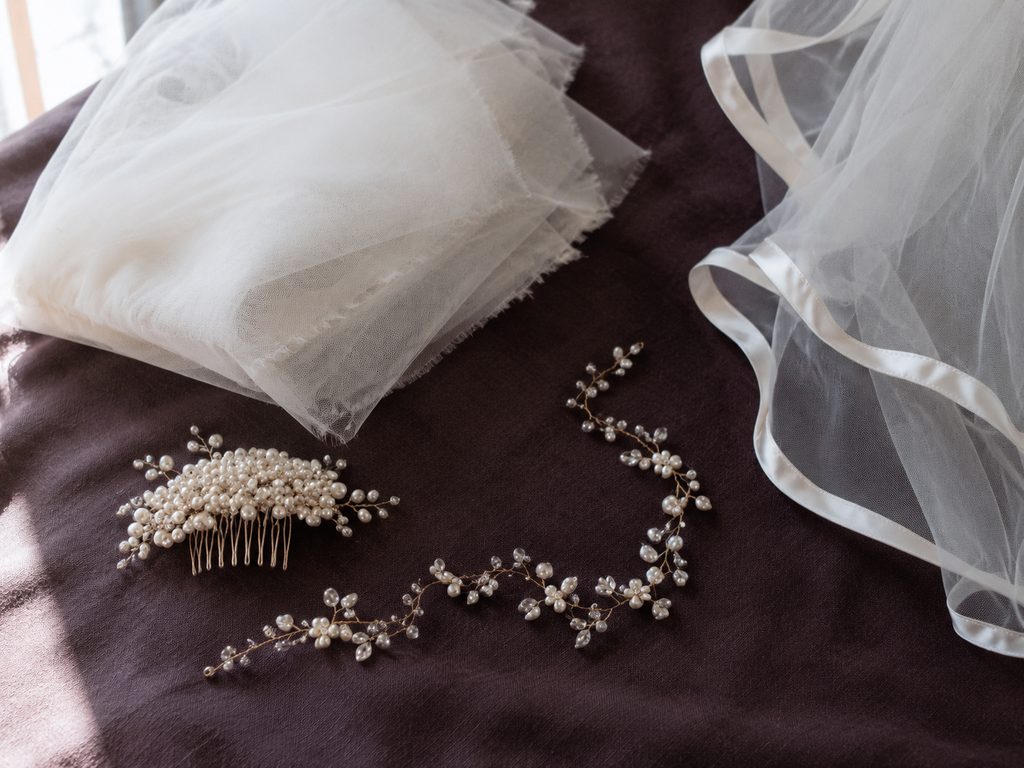 Veils and hair pieces on plum linen: two folded veils, a pearl comb and a crystal hair vine.